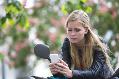 Young woman using mobile phone while leaning on motor scooter