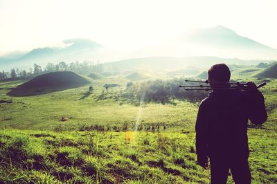 Rear view of man holding tripod while standing on grassy field