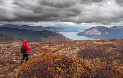 Rear view of woman hiking on mountain against cloudy sky