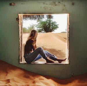 Side view full length of woman sitting at window in abandoned room