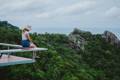 Side view of woman sitting on bench against mountain