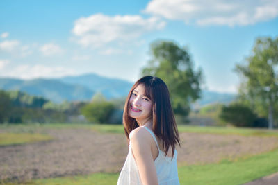 Young woman standing on field against sky