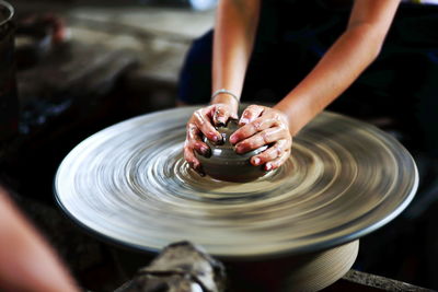 Midsection of woman shaping earthenware on pottery wheel