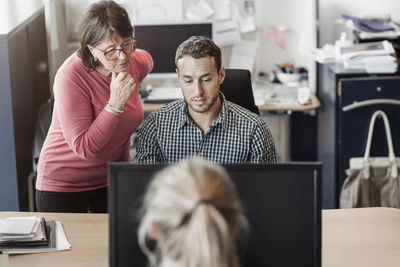 Colleagues using computer at desk in office