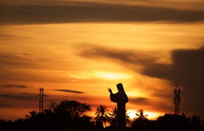 Silhouette man standing by tree against orange sky