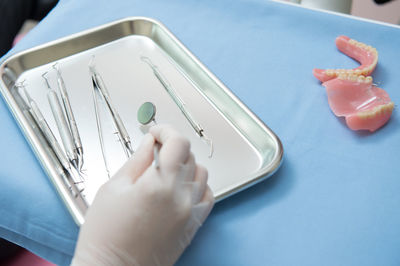 Cropped hand of dentist holding dental equipment in tray on table