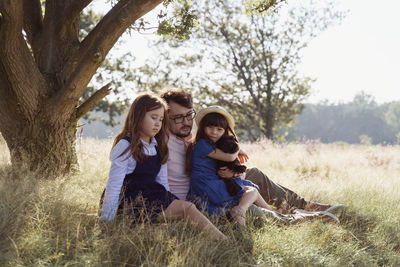 Father with two children and poppy sitting on a field under the tree