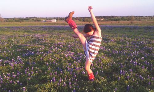 Cheerful girl raising foot amidst purple flowers blooming on field