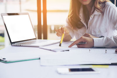Midsection of woman using mobile phone while sitting on table