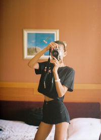 Young woman photographing while standing on bed at home