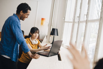 Female programmer explaining to male coworker over laptop on desk in office