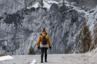 Back view of female hiker wearing winter clothes, walking on gravel path in mountains