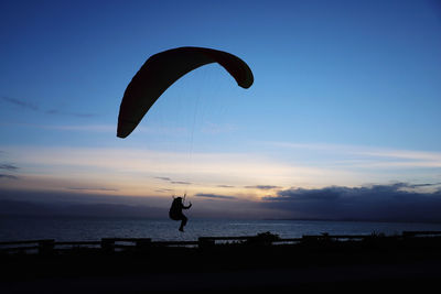 Silhouette person paragliding over sea against sky during sunset