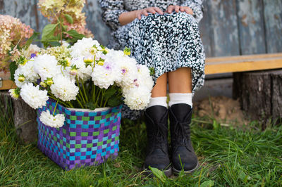 A basket of dahlias and hydrangeas stands near a bench, a man's feet