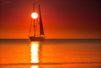 Sailboat sailing on sea against orange sky