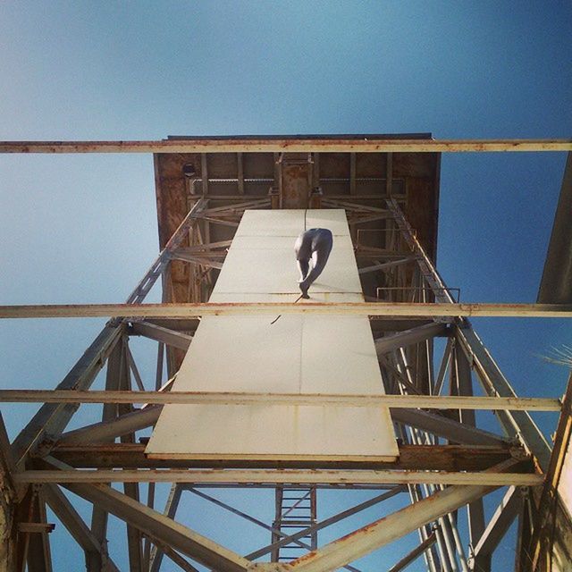 low angle view, clear sky, built structure, architecture, connection, bird, metal, blue, bridge - man made structure, sky, copy space, day, animal themes, one animal, engineering, outdoors, metallic, animals in the wild, wildlife, no people