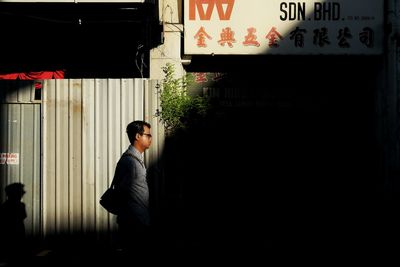 Side view of young man standing against wall