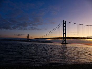 Suspension bridge over sea against sky during sunset