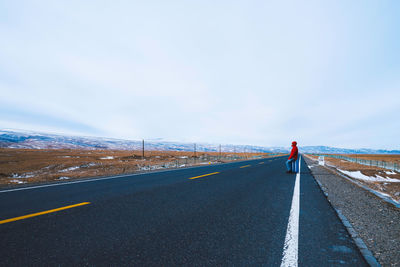 Man sitting on luggage over road against sky