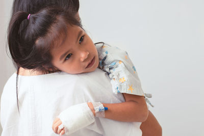 Mother carrying sick daughter against wall in hospital