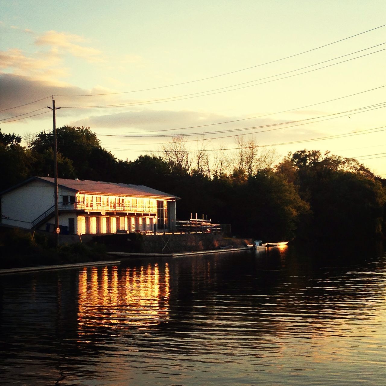 water, waterfront, sky, power line, built structure, sunset, architecture, building exterior, river, reflection, tree, connection, electricity pylon, cable, transportation, cloud - sky, lake, nature, electricity, silhouette