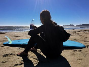 Rear view of woman sitting on beach against clear sky