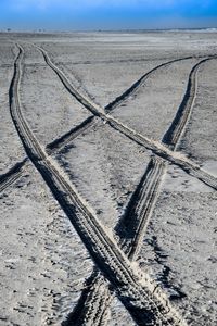 Tire tracks on sand at beach against sky