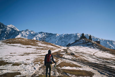 Rear view of person walking on snowcapped mountain against clear sky