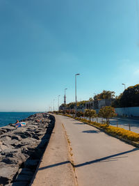 Road by sea against clear blue sky