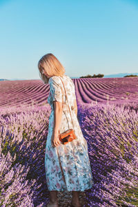 Rear view of woman standing on a lavender field against sky