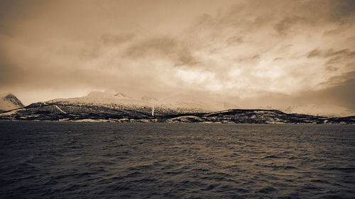 Scenic view of sea by snowcapped mountains against sky