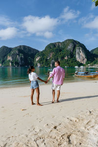 Rear view of friends standing on beach against sky