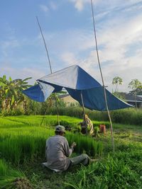 Rear view of man sitting on field against sky