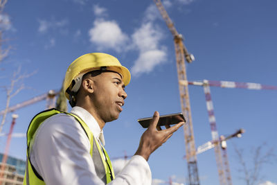 Engineer talking on smart phone through speaker at construction site on sunny day