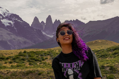 Portrait of young woman wearing sunglasses standing on mountain against sky