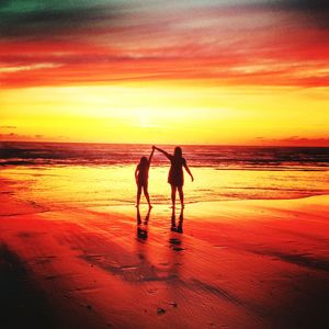 Rear view of silhouette mother with daughter standing at beach during sunset