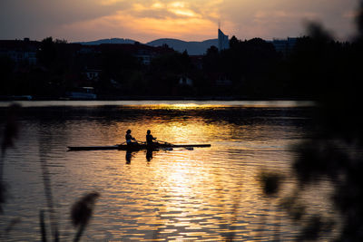 Silhouette people in river against sky during sunset