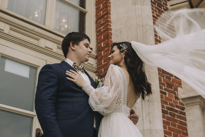 Smiling bride embracing groom in front of building