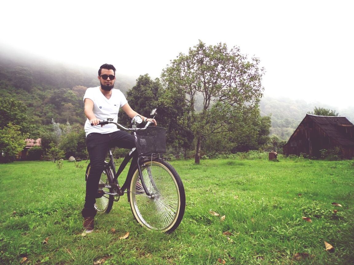 bicycle, full length, lifestyles, grass, land vehicle, transportation, mode of transport, leisure activity, casual clothing, young adult, tree, person, side view, riding, field, young men, standing, day