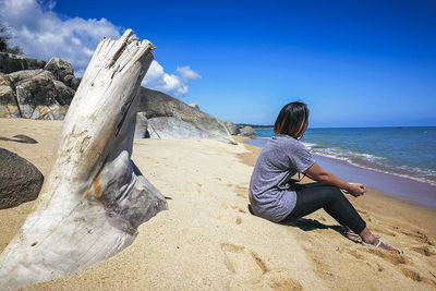 Man sitting on rock by sea against sky