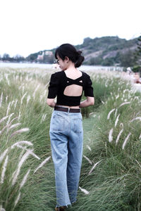 Full length of young woman standing on field in backless top and jeans 