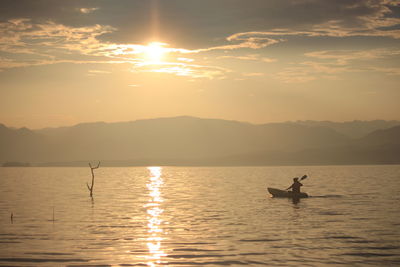 Silhouette man in sea against sky during sunset