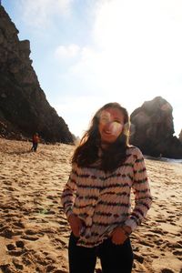 Portrait of smiling woman standing at sandy beach against sky