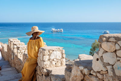 Happy african american woman in yellow dress and sun hat enjoys view of coast of red sea 