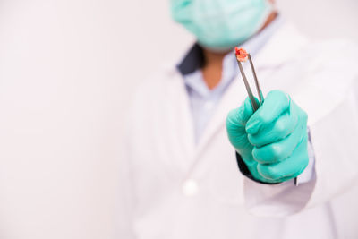 Midsection of doctor wearing gloves holding tooth in equipment