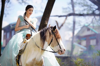 Low angle view of young woman riding horse in forest