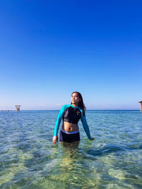 Smiling young woman in sea against clear blue sky