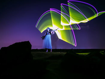 Rear view of woman standing against sky at night