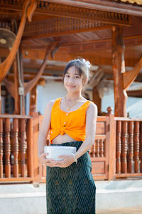 Portrait of young woman standing against built structure