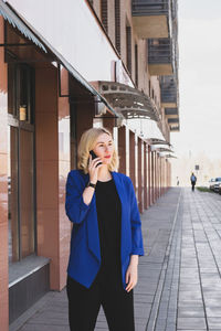 Full length of woman standing on mobile phone in city